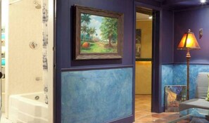 Relax in a stylish room with a tropical landscape painting, glass coffee table, and cozy seating area.