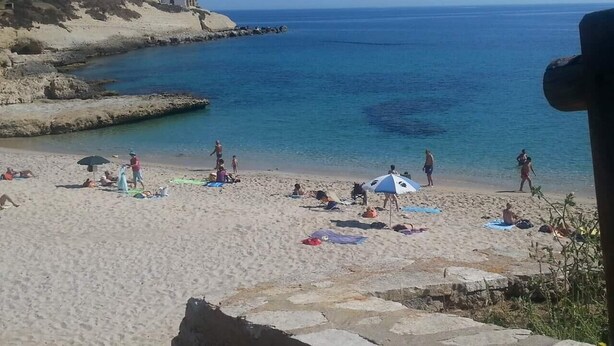 Una playa con gente tomando el sol, sombrillas y un litoral rocoso.
