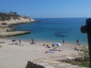 A beach with people sunbathing, umbrellas, and a rocky shoreline.
