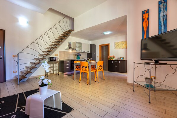A modern living space with a staircase, dining area, kitchen, and a flat-screen TV.