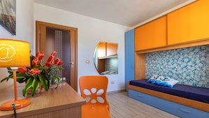 Una habitación con una cama, un escritorio, una silla, una lámpara y un jarrón de tulipanes.