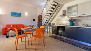 Una cocina moderna con una escalera, un comedor con sillas anaranjadas y un sofá rojo.