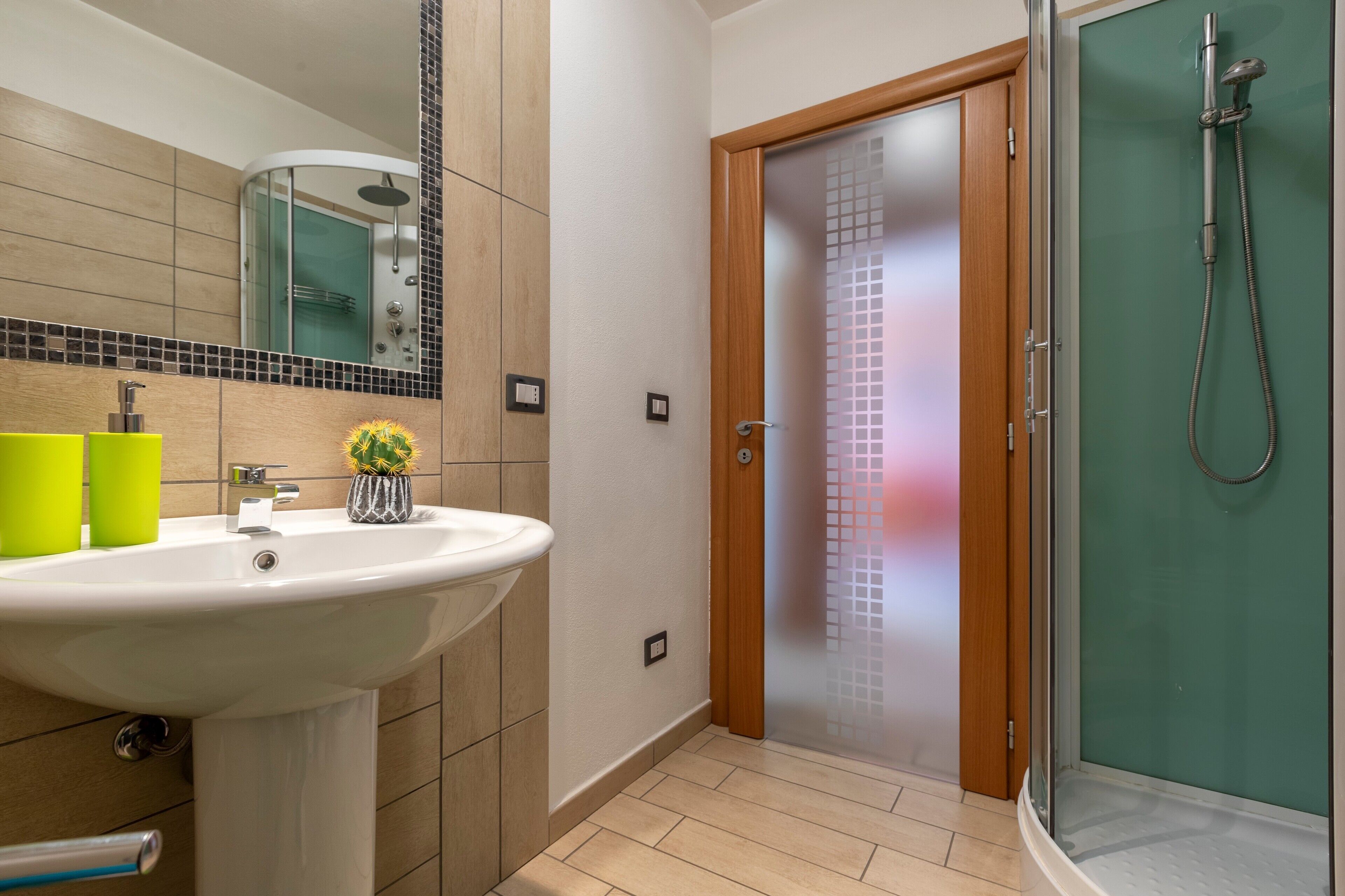 Bagno con lavandino, specchio, doccia e porta in vetro satinato.