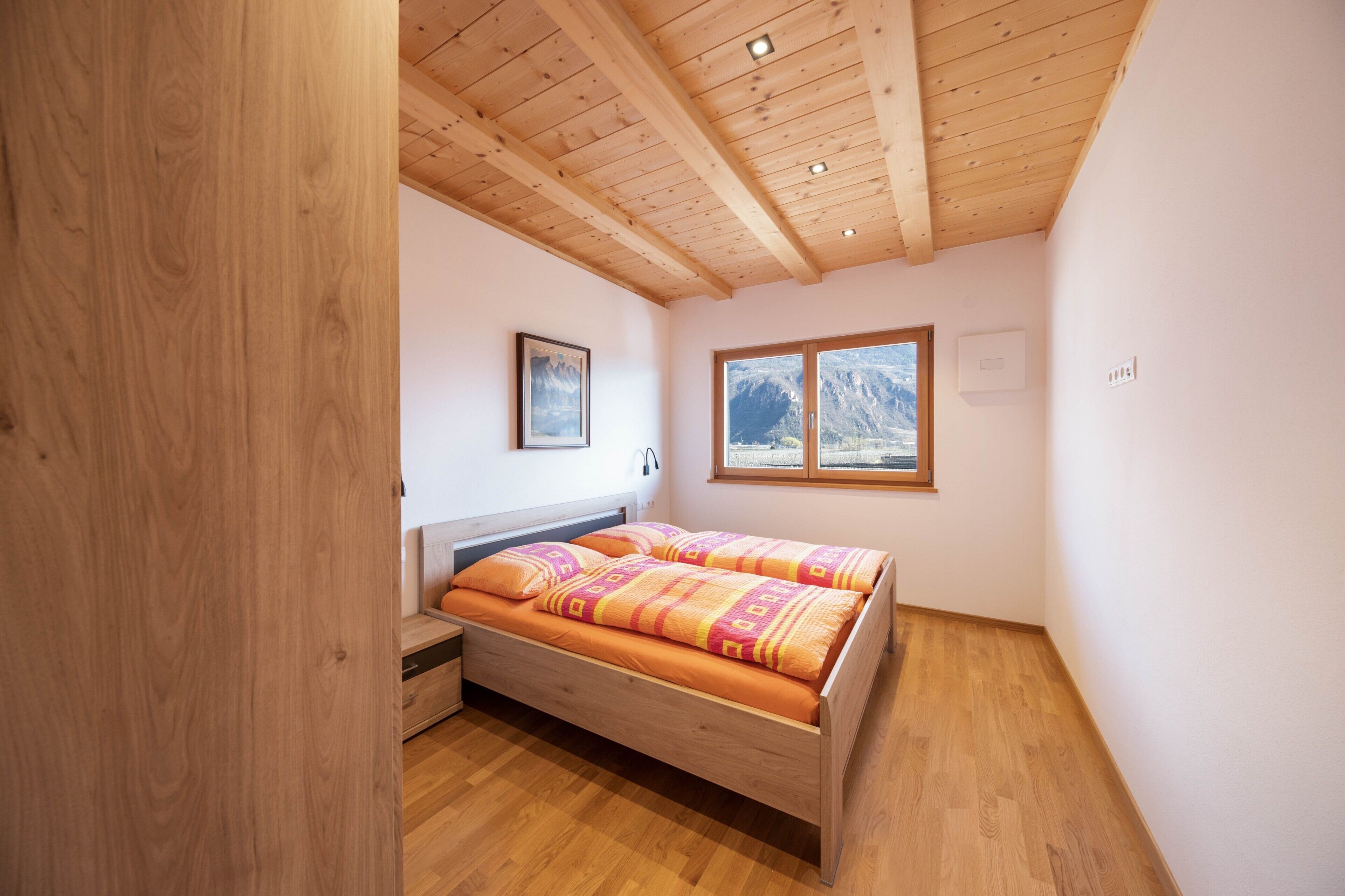 Ein Schlafzimmer mit einem Holzbett, einem Fenster mit Bergblick und einer Holzbalkendecke.
