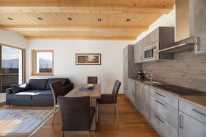 A modern kitchen with wooden ceiling, a dining area with a table and chairs, and a sofa. - Bright Apartment "1 Weger" with Panoramic Mountain View, Wi-Fi & Balcony (Andrian)