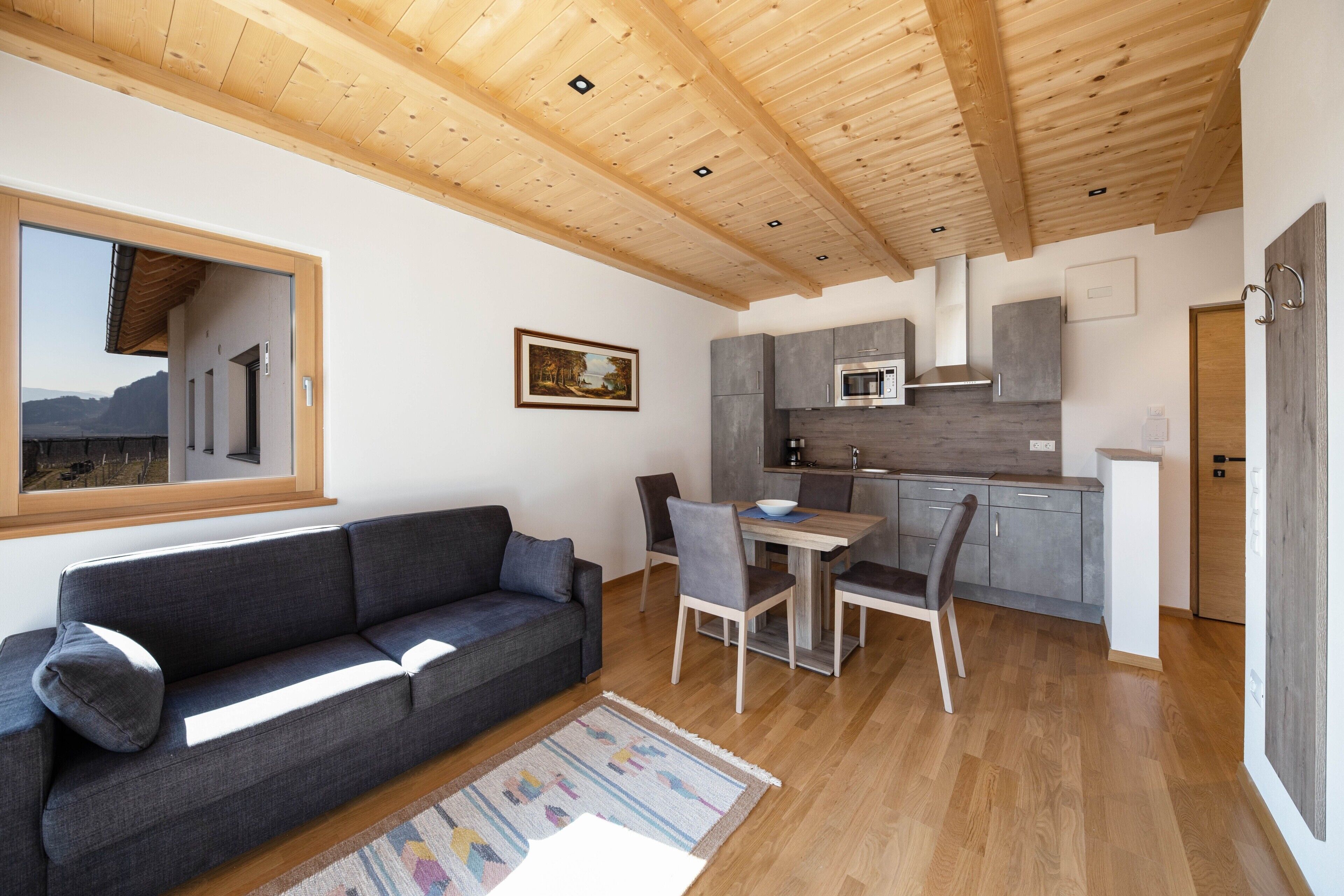 Et moderne interiør med træloft, sofa, spisebord med stole, et køkkenområde og et vindue med udsigt.