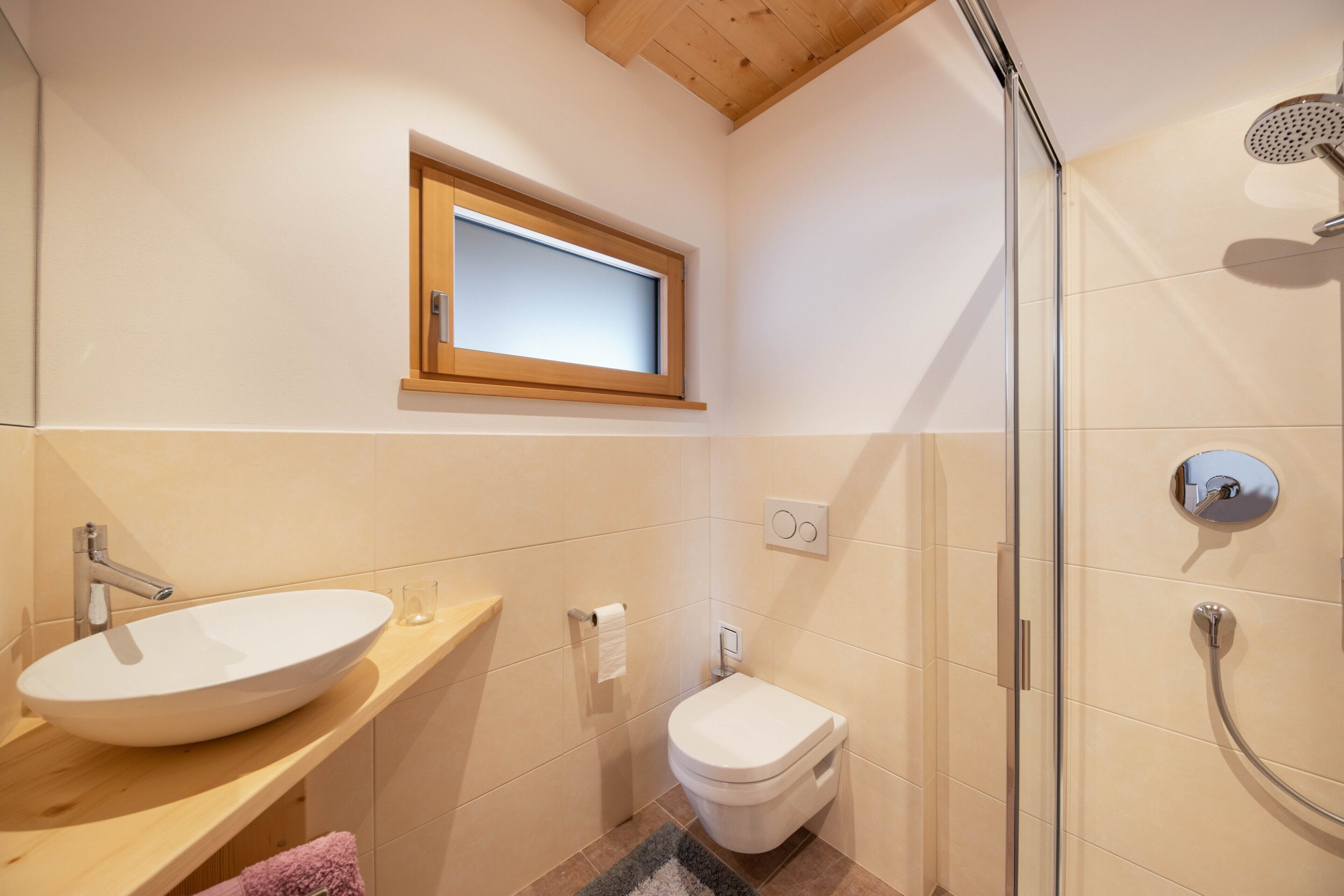 Une salle de bain avec un meuble-lavabo en bois, un lavabo blanc, des toilettes et une douche à parois de verre.