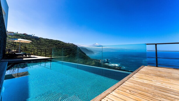 Ein Pool im Infinity-Stil mit einer Holzterrasse, mit Blick auf eine Küstenlandschaft und ein Gebirge.