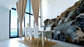 Ein Essbereich mit Tisch und Stühlen, ein großes Fenster mit Vorhängen und einer Felswand.