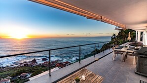 Ein Balkon mit Meerblick und Sonnenuntergang, ein Tisch mit Stühlen und ein Grill.