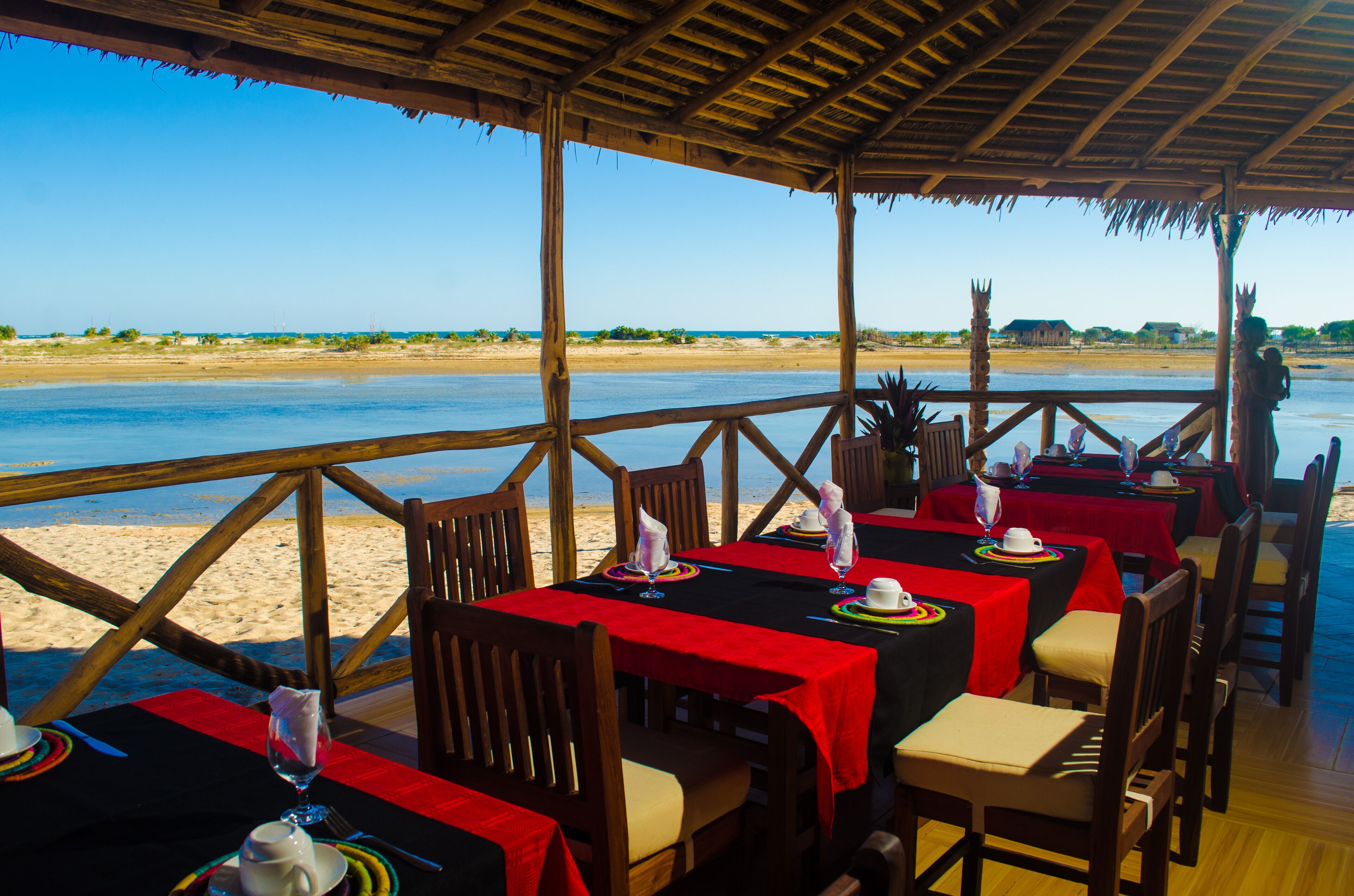Un espace de restauration en plein air avec des tables disposées pour deux personnes, donnant sur une plage.
