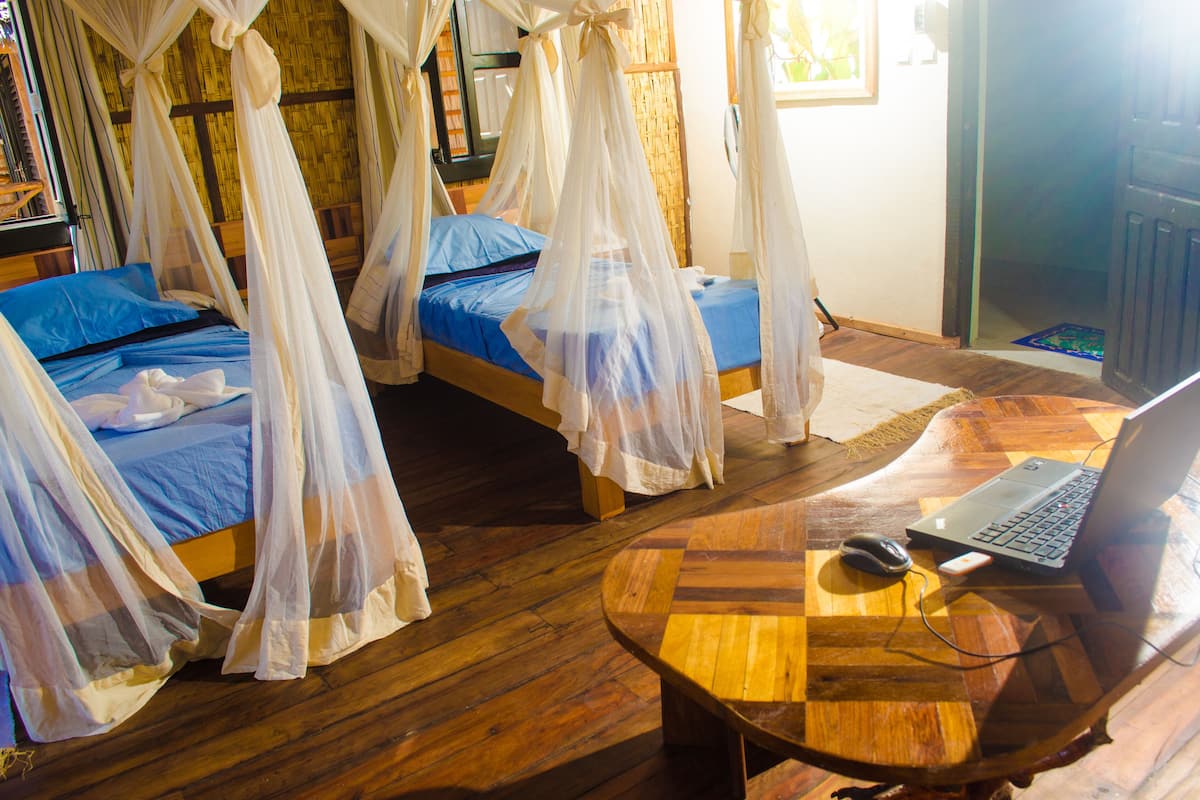 A room with two beds, each with a canopy, a wooden table with a laptop, and a computer mouse.