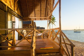 A wooden deck with chairs and a table, overlooking a beach with boats and palm trees. - Belo Beach (Belo Sur Mer)