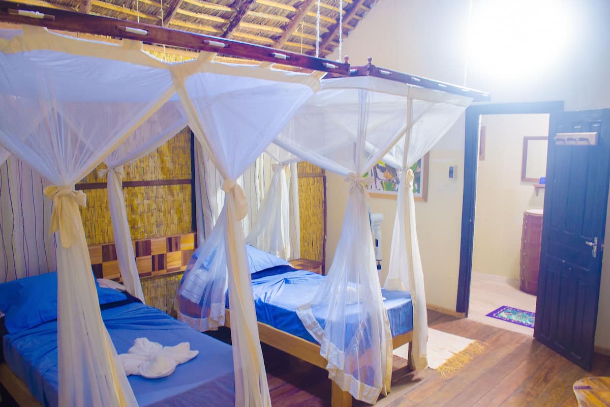 A room with four beds, each with a canopy. There is a wooden door and a small window visible.