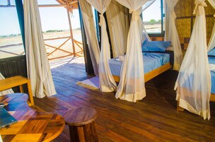 Una habitación con una cama bajo un dosel, suelo de madera y vista a la playa.