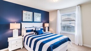 A bedroom with a bed, two bedside tables, a window with blinds, and wall art.