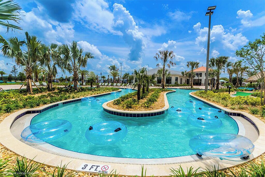 A swimming pool with multiple lanes, surrounded by palm trees and a building in the background.