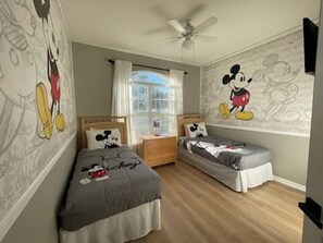 A bedroom with two beds, a ceiling fan, and Mickey Mouse-themed decor.