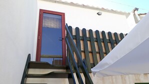Eine Treppe führt zu einer Tür mit Glasschiebeelement, einer weißen Markise und einem Bambuszaun.