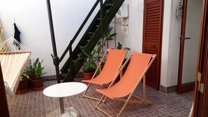 Eine Terrasse mit Pflasterboden, zwei orangefarbene Klappstühle, einem runden Tisch, einer Hängematte und Topfpflanzen.