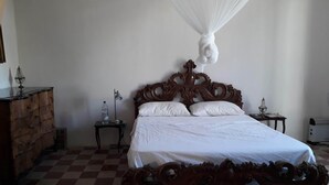 Ein Schlafzimmer mit einem Holzbett, weißer Bettwäsche, einem karierten Boden, einem Nachttisch mit Lampe und einer Kommode.