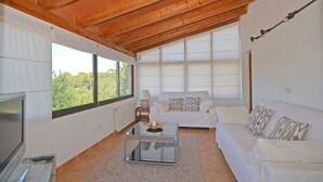 Un salón amplio con un sofá blanco, una mesa de centro de cristal y una televisión.