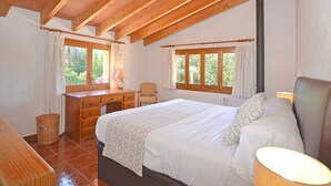 Un dormitorio con techo de madera, una cama con ropa de cama blanca, un escritorio con lámpara y una silla.