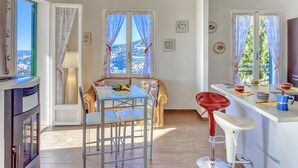 Un coin repas accueillant avec une table et des chaises, un tabouret de bar rouge et une vue sur la ville par les fenêtres.