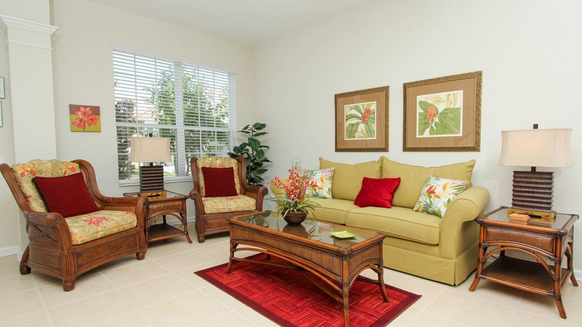 A living room with a beige sofa, two armchairs, a coffee table, and two side tables with lamps. There are two framed botanical prints on the wall.