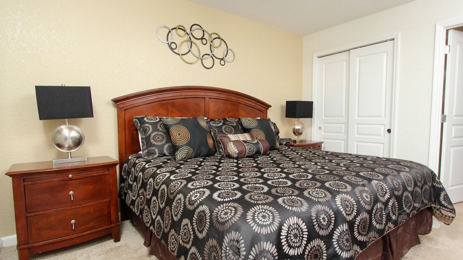 A bedroom with a large bed, two nightstands, a wooden dresser, a wall art piece, and a white door.