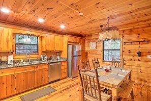 L’intérieur d’un chalet en bois comprend une cuisine équipée d’armoires en bois, d’un réfrigérateur en acier inoxydable et d’une table à manger avec des chaises.