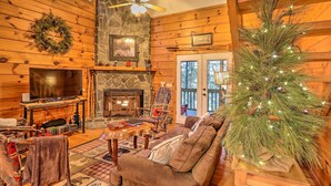 A cozy log cabin interior with a stone fireplace, a television, and a Christmas tree. - Luxe Fightingtown Creek Cabin: 2 King Suites & Spa (Epworth)