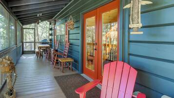 A covered porch with wooden chairs and tables, a wooden birdhouse, and a porch angel decoration.