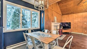Un coin repas avec une table en bois, des chaises blanches et une grande fenêtre donnant sur des arbres couverts de neige.