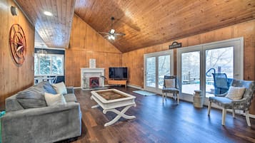 Un salon spacieux avec un plafond en bois, une cheminée, un téléviseur et une grande fenêtre.