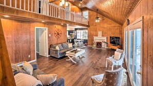 A spacious living area with a high ceiling, wooden walls, a balcony, and a fireplace. - Hot Tub: Secluded Hideaway on Sleepy Hollow Lake (Athens)