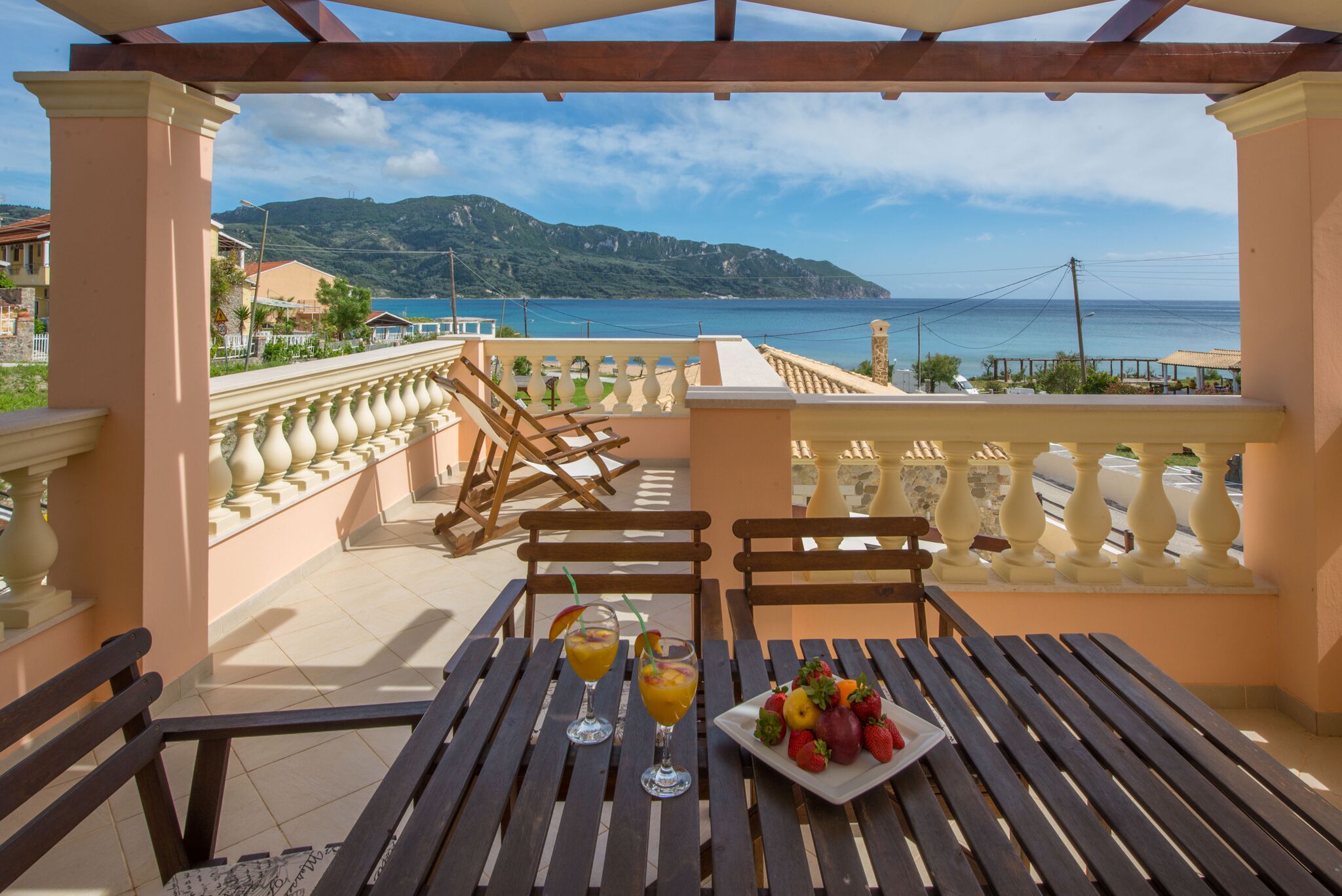 A balcony with a table set for two, featuring a fruit platter and two drinks.