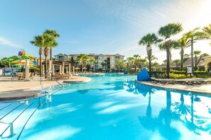 Une piscine entourée de bâtiments d’hôtel, avec des chaises longues et des palmiers.