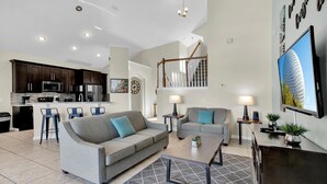 A modern living room with a grey sofa, a coffee table, and a TV. There is a kitchen area with dark cabinets and a microwave. A staircase leads to an upper level. - New Listing! Windsor Palms Resort, 3mi to Disney & 13mi to Universal - GRH438784 (Kissimmee)