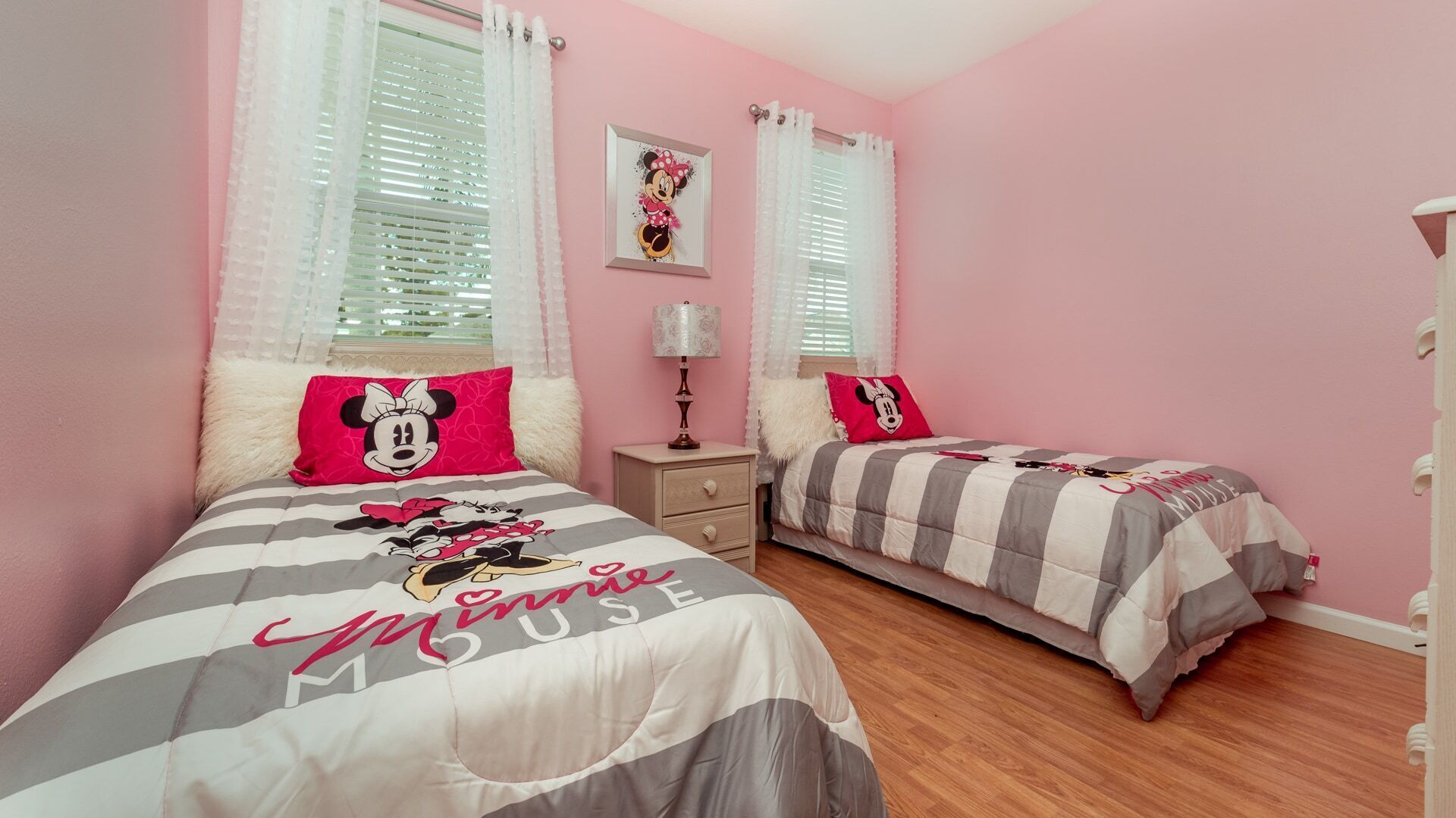 Une chambre à coucher décorée dans des tons de rose, avec deux lits, chacun agrémenté de linge de lit à l’effigie de Minnie Mouse.