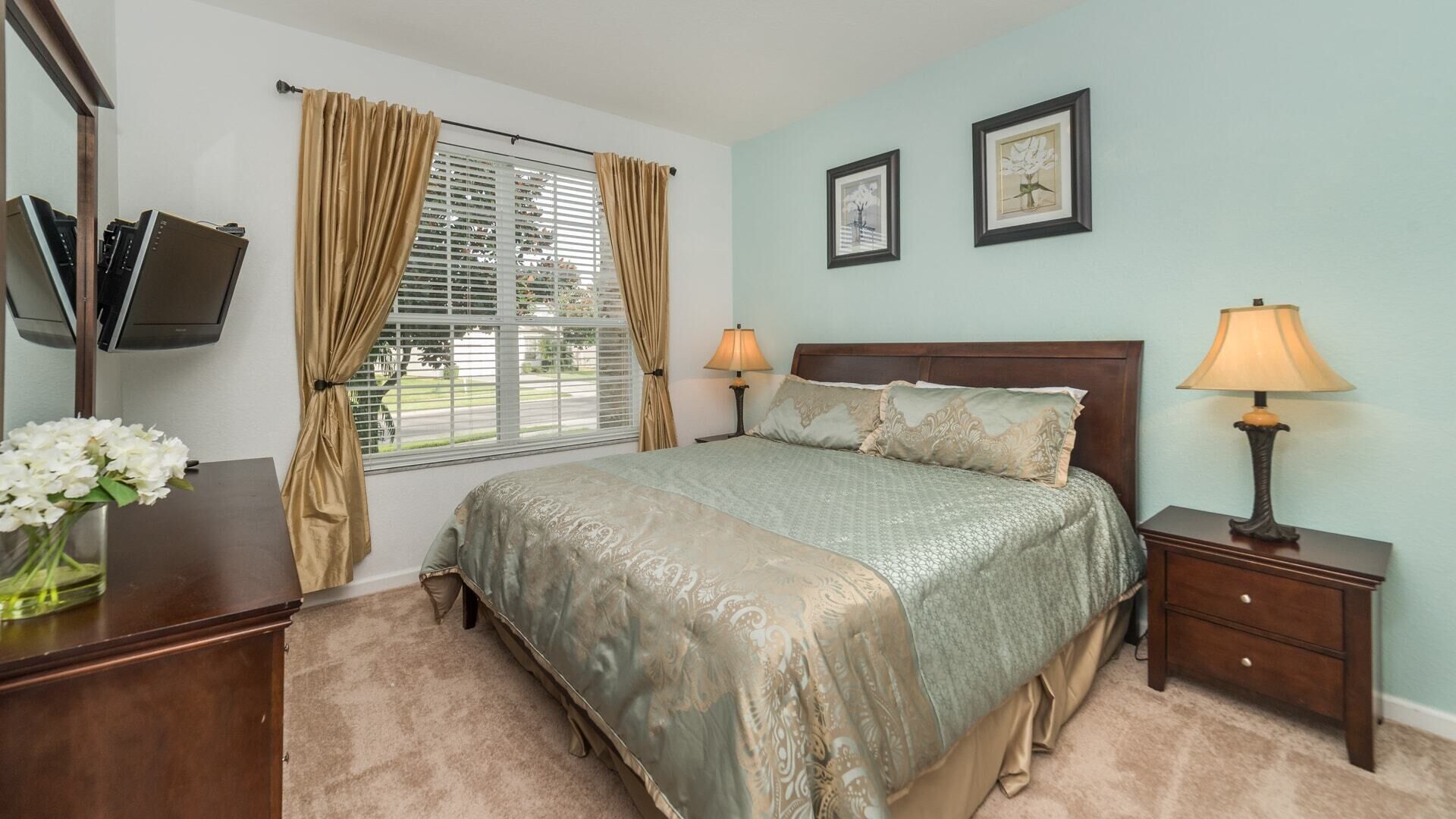 A bedroom with a bed, bedside lamps, a nightstand, a dresser, a mirror, and a window with curtains.