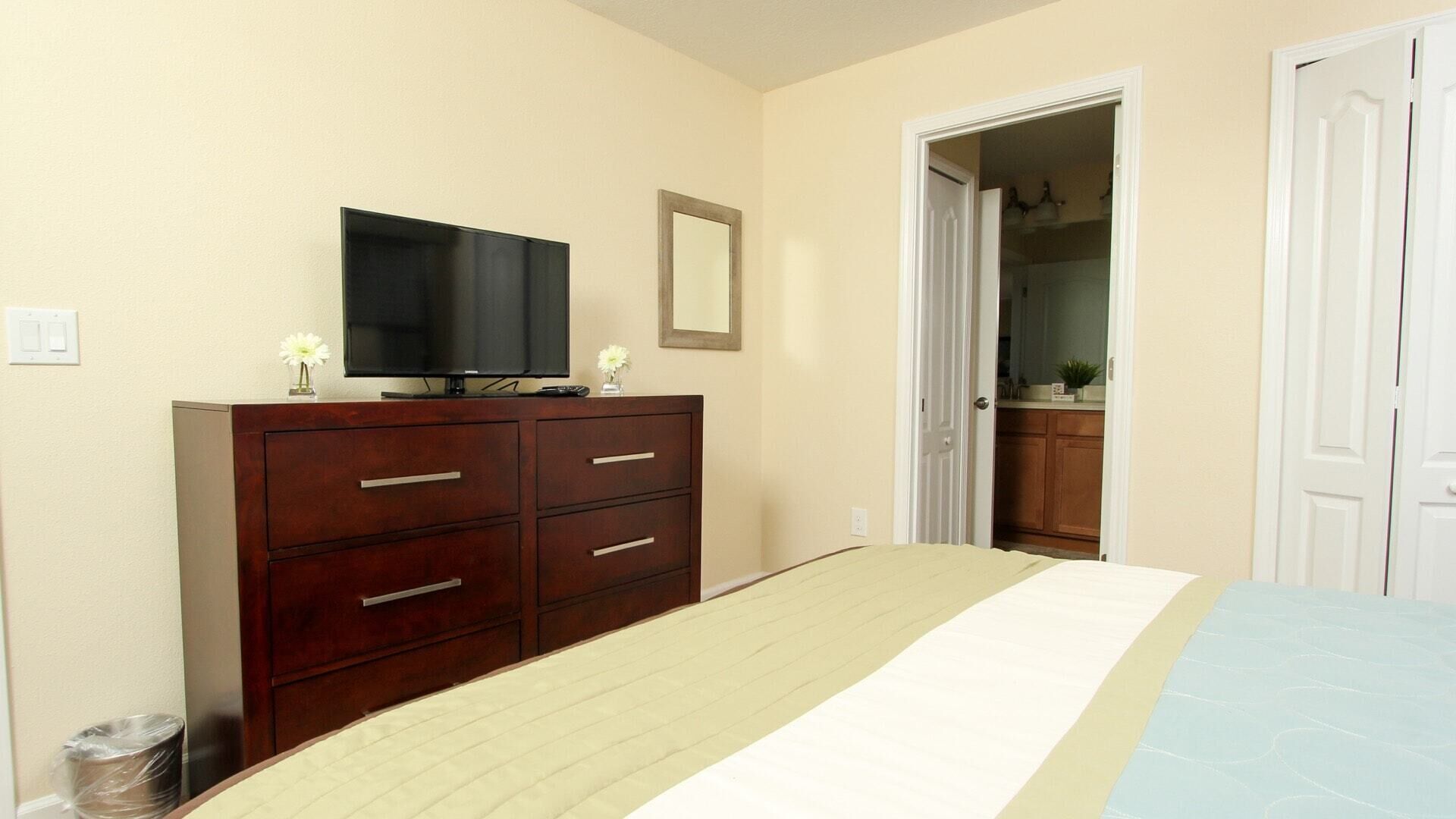 A bedroom with a bed, a dresser, a television, and a mirror.