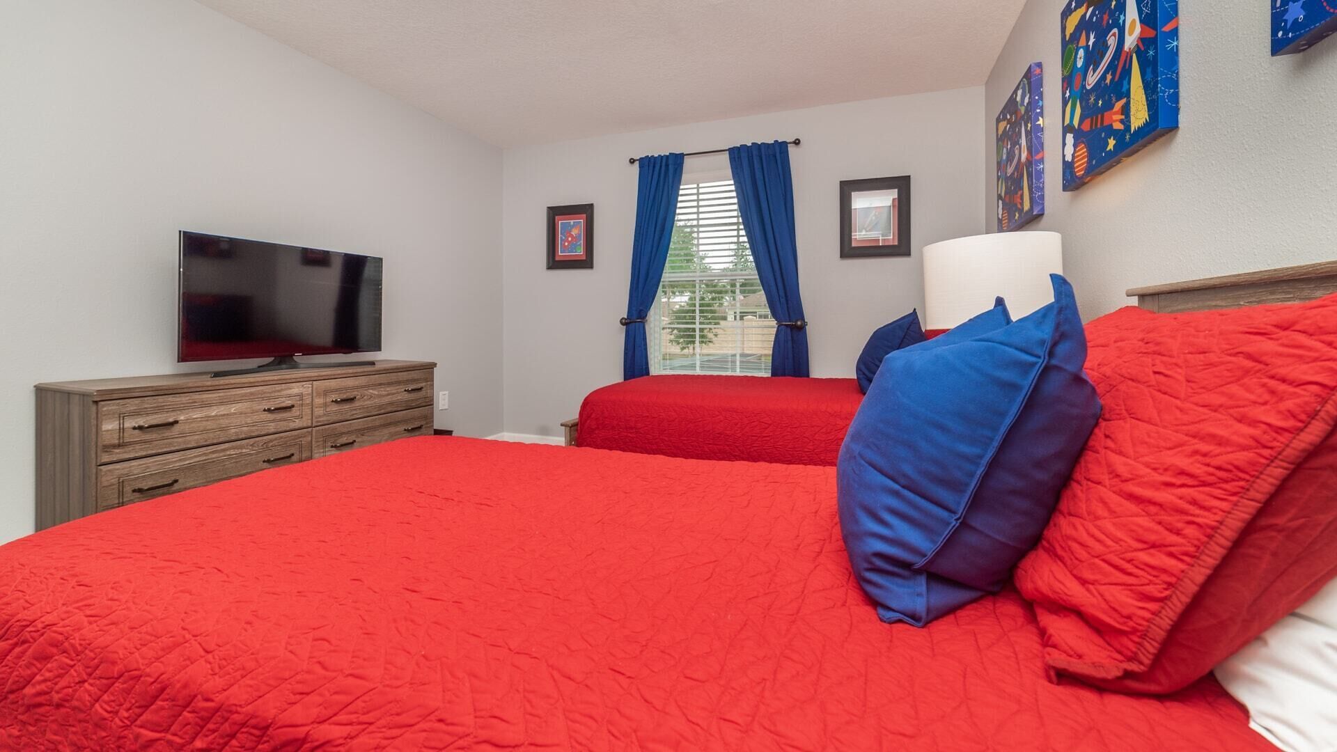 Een slaapkamer met een groot bed, een televisie op een houten dressoir en een raam met blauwe gordijnen.