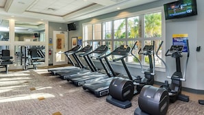 A fitness center with treadmills, elliptical machines, and a TV screen displaying sports.