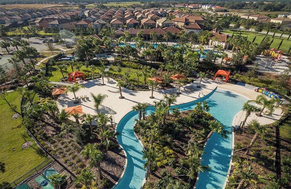 Vista aérea de un resort con una piscina serpenteante, palmeras y una zona residencial al fondo.