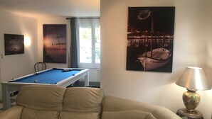Un salon avec une table de billard, un canapé beige et une lampe.