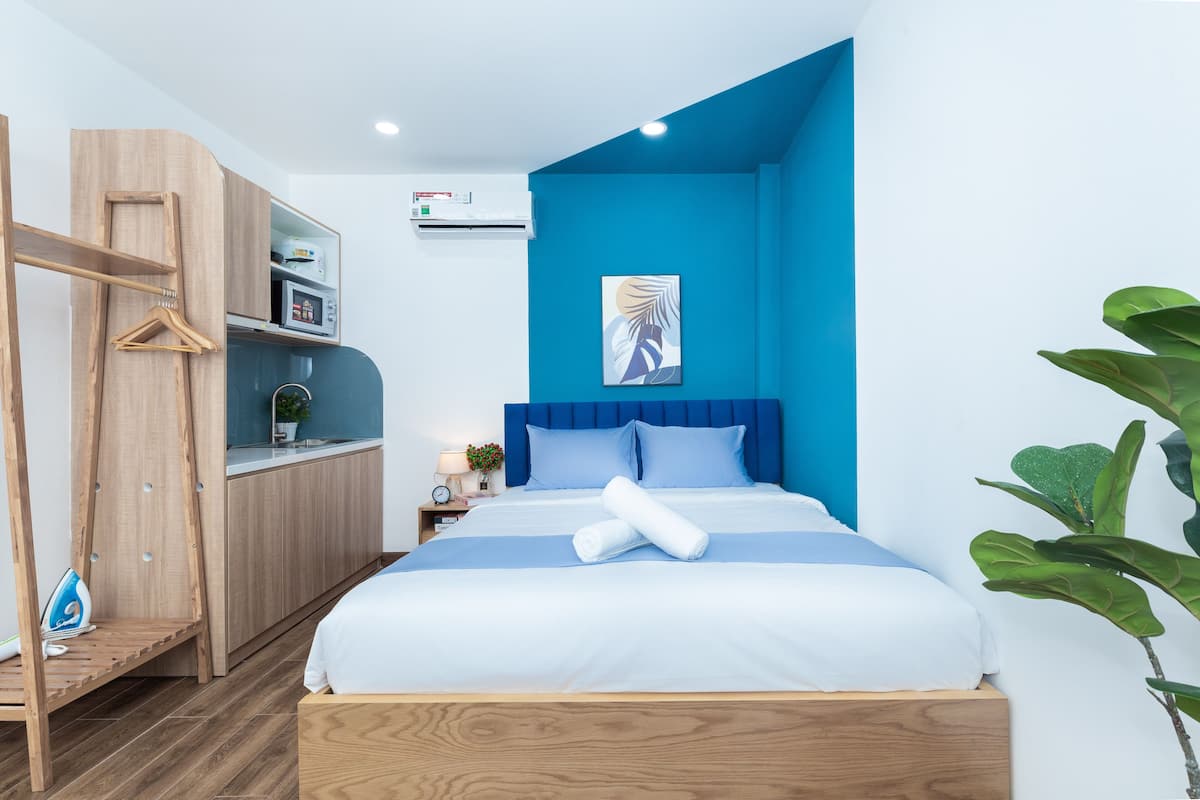 Een moderne hotelkamer met een bed, een houten kledingkast, een nachtkastje en een blauwe accentmuur.