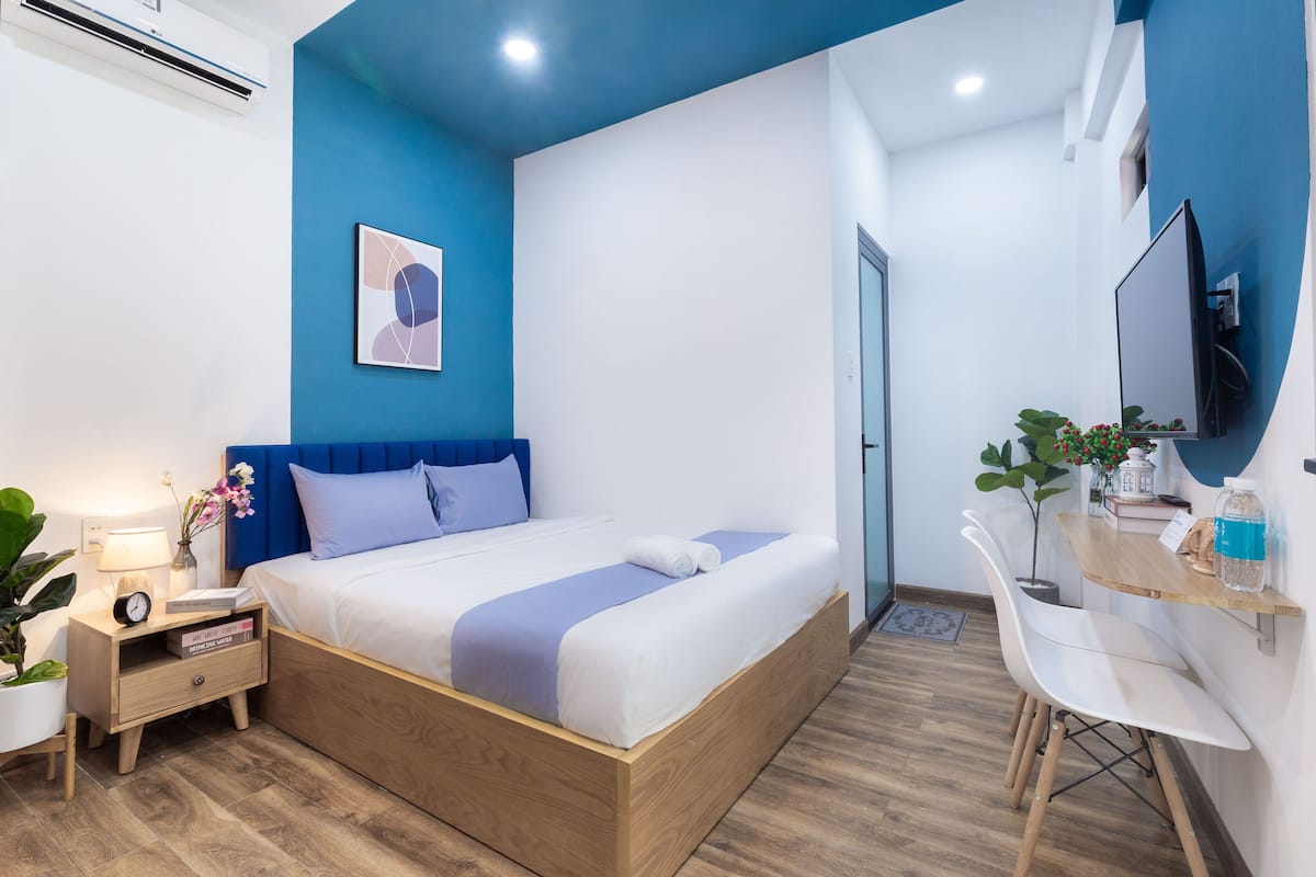 Een moderne slaapkamer met een bed, nachtkastje, lamp en een televisie op een houten bureau.
