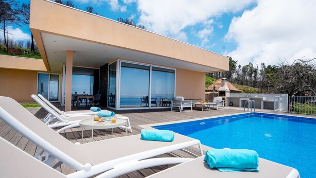 En modern villa med en swimmingpool, solstolar och en matplats med utsikt över havet.