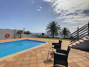A swimming pool with tiled flooring, a lifebuoy, and outdoor seating with drinks. - Villa Prainha by LovelyStay (Canical)